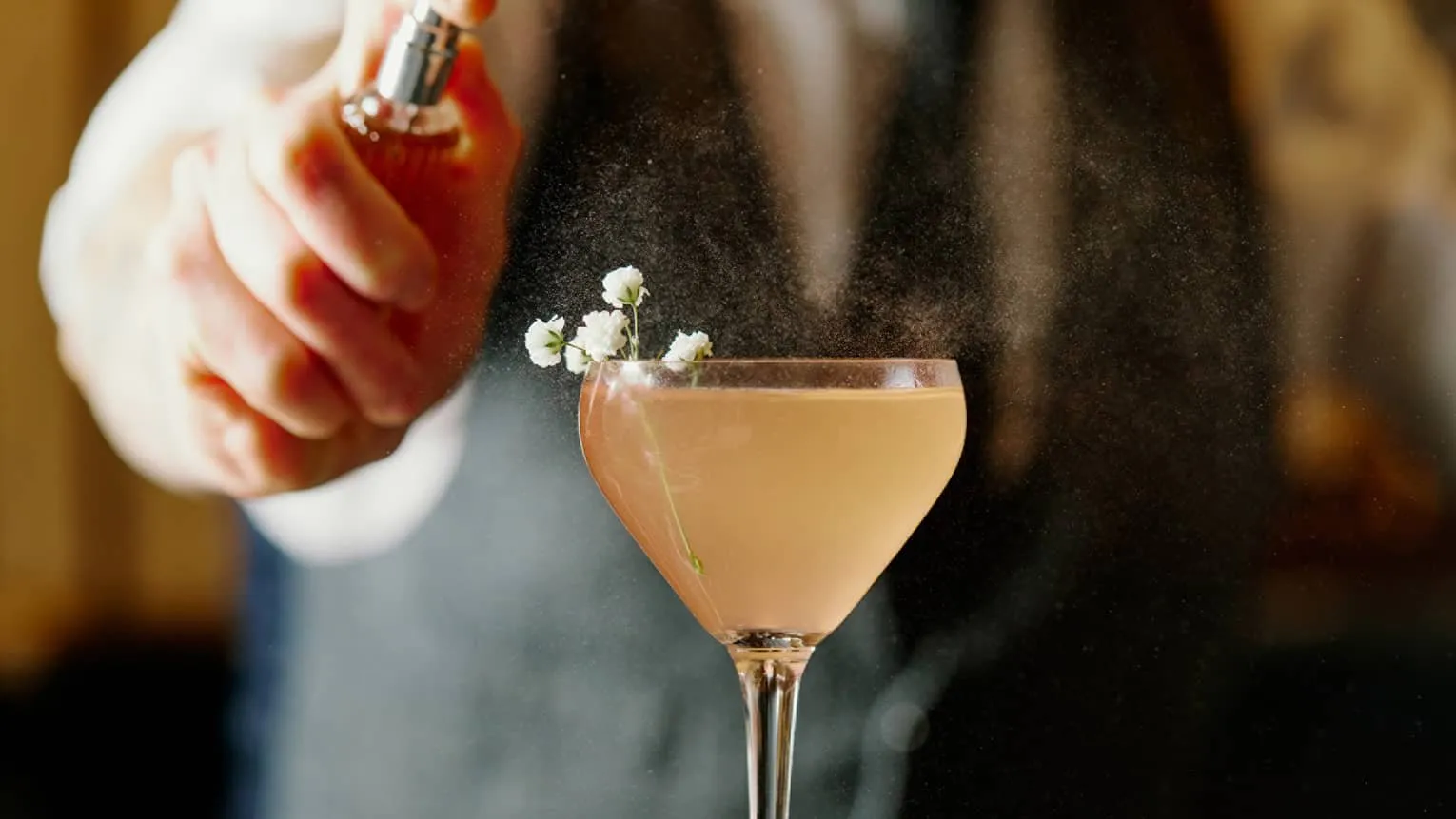 A bartender sprays a pale cocktail garnished with small flowers at Trifecta