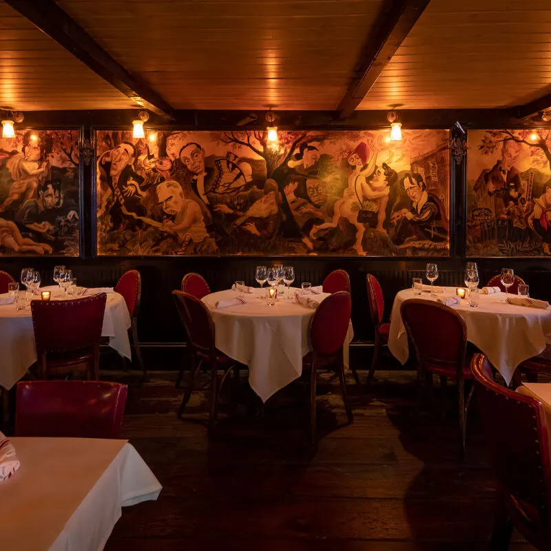 Warmly lit dining room at The Waverly Inn with red chairs and a mural
