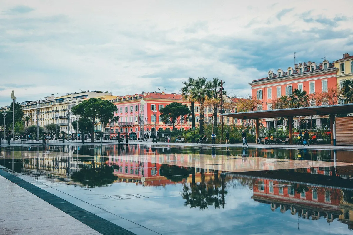 Pastel buildings and palms reflected in water in Nice